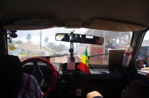 Prendre un taxi sénégalais est une expérience à vivre : klaxon, porte qui ne ferme pas, plancher troué, possibilité de monter à 7 dans une 5 places....