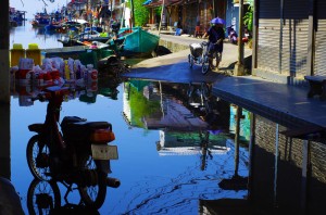 Lorsque la marée est haute, l’eau monte jusque dans les rues du village. Ici une photographie d’une scène quotidienne typiquement thaïe. L’accoutrement des cyclistes en particulier donne le sourire.
