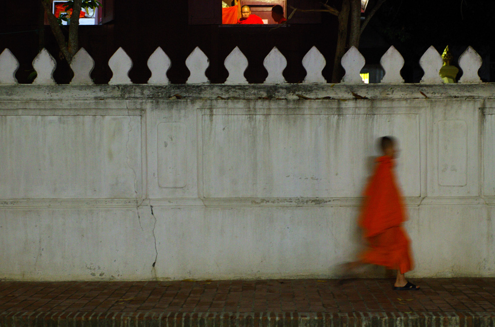 Il est déjà 21 h et les moines ont un rythme de vie très strict, se lèvent très tôt, méditent et prient de longues heures le jour durant. C’est donc le moment de rentrer au « Wat » temple … Sur le haut de la photographie, on aperçoit un maître bouddhiste guettant ces jeunes élèves, même si l’heure n’est pas la première des priorité au Laos, celui-ci serait t-il un peu en retard ?