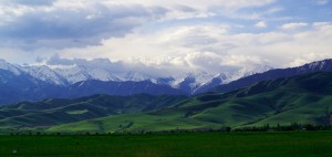 Le Kirghizstan après avoir passé les premières montagnes : une large plaine verte avec une grande chaîne de sommets enneigés en fond. C'est là bas que nous allons nous évader...