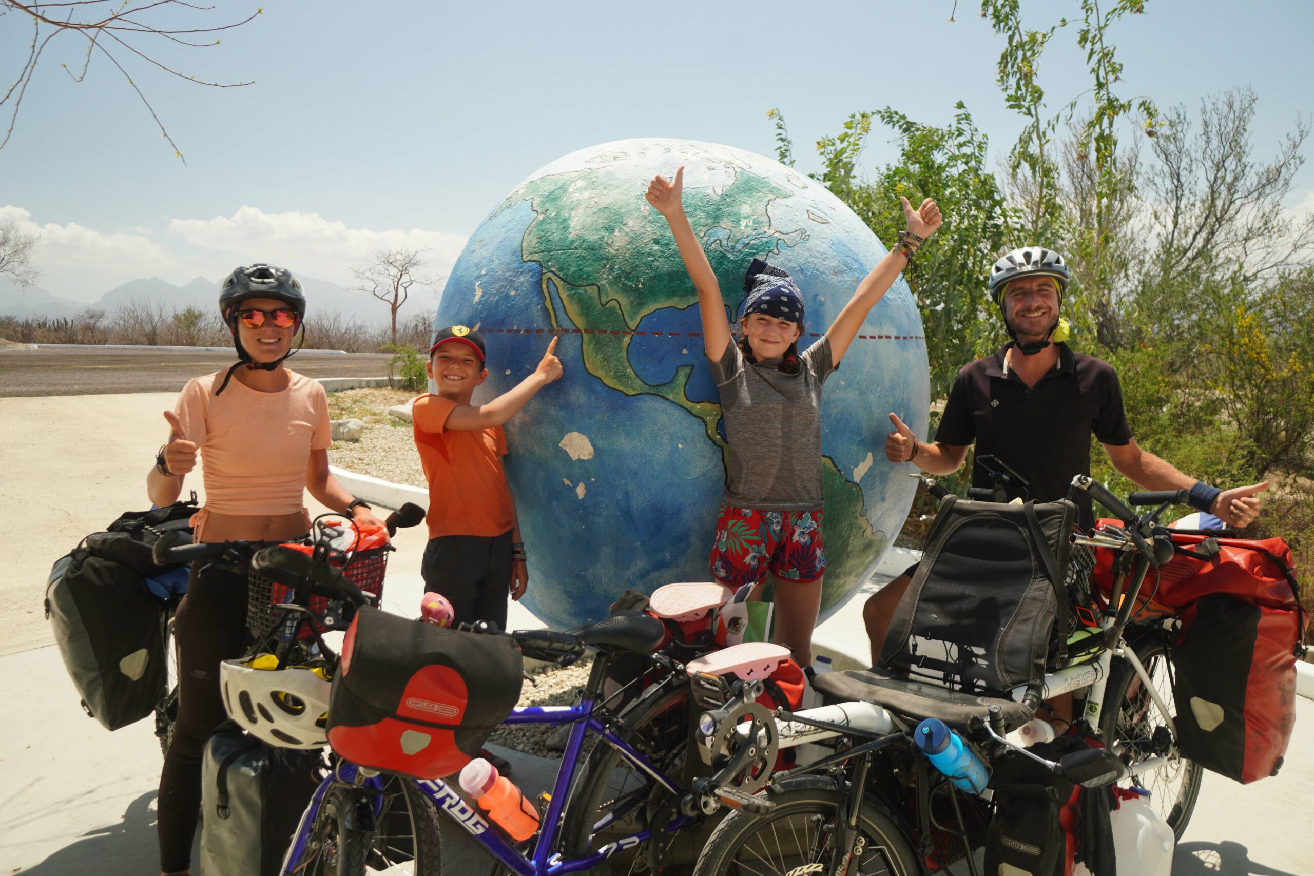 Aurélie, Côme, Clélia et Célian posent avec leurs vélos devant un globe terrestre